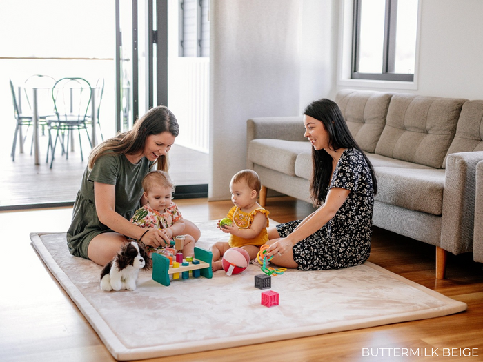 Two babies and two mothers sit on Relax Mat with toys