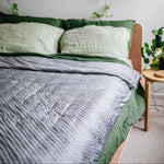 Bedroom with green bedding and hanging plants on a white wall.