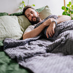 Man lying in bed with plants around, looking peaceful.