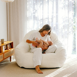 An oversized white foam chair with a removable cover, where a person is seated comfortably holding a baby.