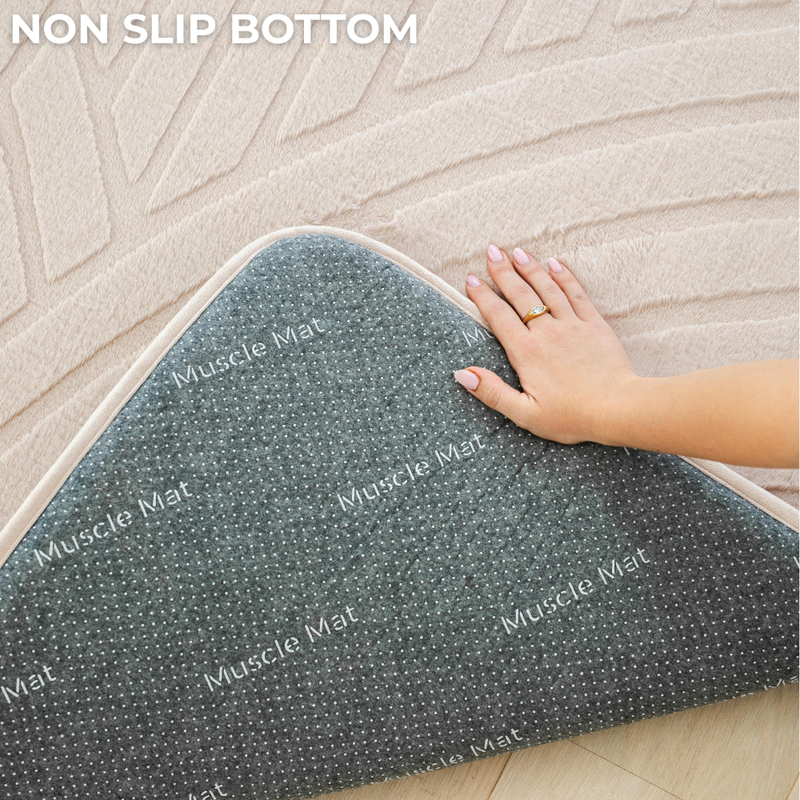 Gray 'Muscle Mat' with a hand pressing down on it, on a textured floor.