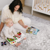 Woman and child reading books on a carpeted floor with a crib in the background