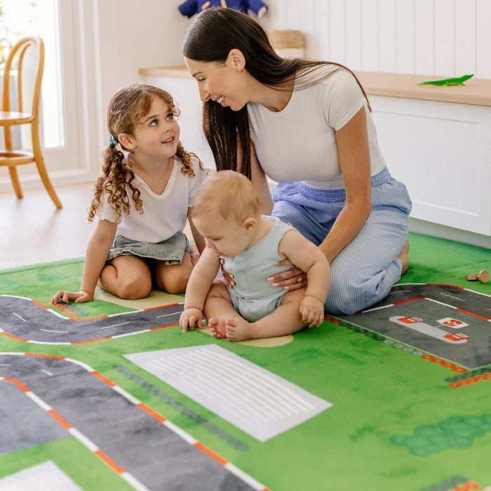 woman with small child and baby on a mat with roads and grass design